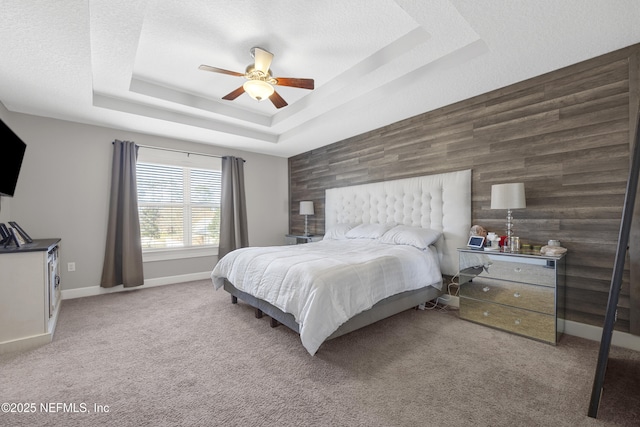 carpeted bedroom featuring ceiling fan, a textured ceiling, a tray ceiling, and wooden walls