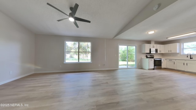 unfurnished living room with ceiling fan, sink, vaulted ceiling, and light hardwood / wood-style flooring