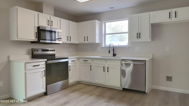 kitchen with appliances with stainless steel finishes, light wood-type flooring, white cabinetry, and sink