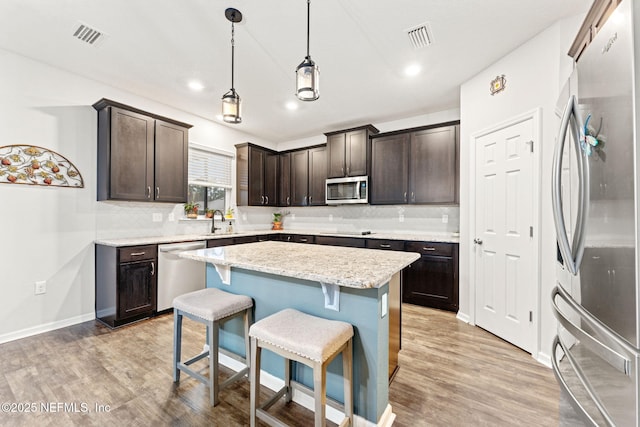 kitchen featuring appliances with stainless steel finishes, dark brown cabinetry, decorative light fixtures, a center island, and a breakfast bar area