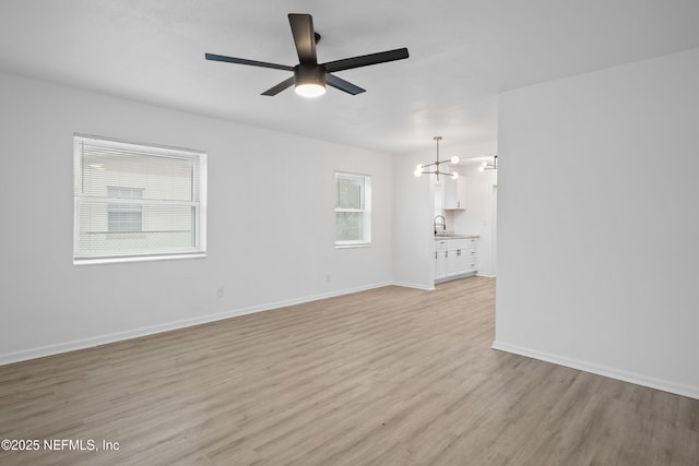 unfurnished living room with light hardwood / wood-style floors, sink, and ceiling fan with notable chandelier