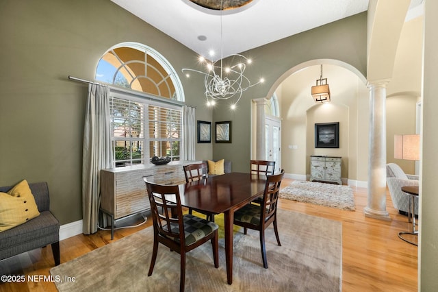 dining area featuring wood-type flooring, decorative columns, high vaulted ceiling, and a notable chandelier