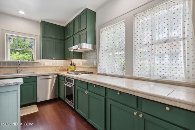 kitchen featuring stainless steel appliances, sink, green cabinets, tile counters, and backsplash