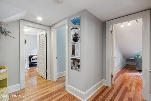 corridor with light wood-type flooring and vaulted ceiling