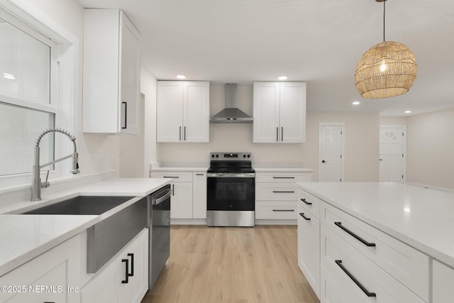 kitchen with wall chimney exhaust hood, decorative light fixtures, white cabinetry, stainless steel appliances, and light hardwood / wood-style flooring