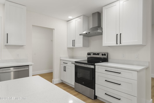 kitchen with light hardwood / wood-style floors, white cabinets, wall chimney exhaust hood, and stainless steel appliances