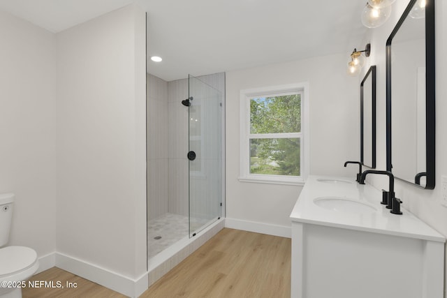 bathroom with toilet, vanity, wood-type flooring, and a tile shower