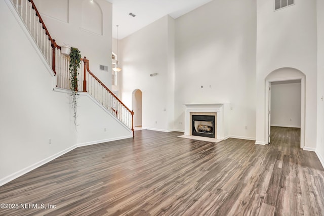 unfurnished living room featuring dark hardwood / wood-style flooring, a tiled fireplace, and a high ceiling