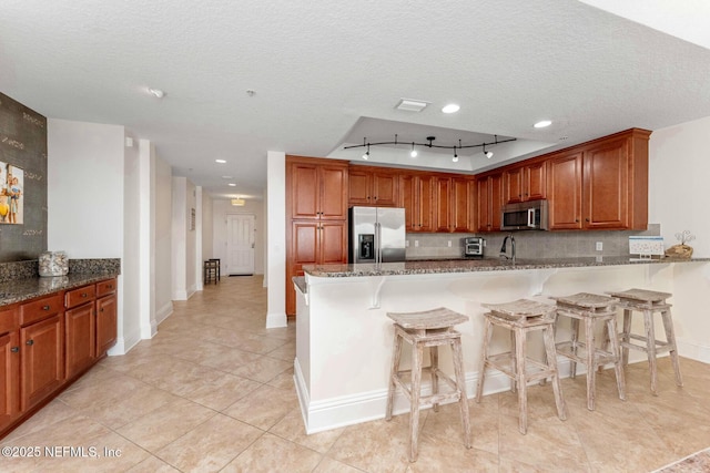 kitchen featuring kitchen peninsula, a kitchen breakfast bar, stainless steel appliances, a textured ceiling, and light stone counters