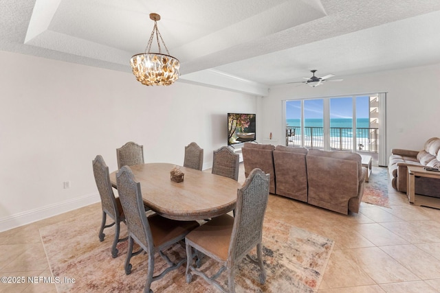 tiled dining space with a water view, ceiling fan with notable chandelier, a textured ceiling, and a raised ceiling