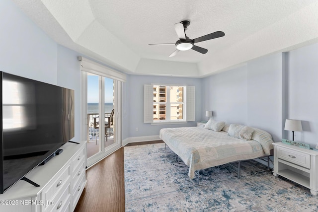 bedroom with ceiling fan, access to exterior, dark hardwood / wood-style floors, a raised ceiling, and a textured ceiling