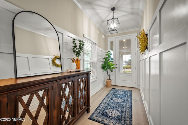 doorway with light wood-type flooring, an inviting chandelier, and crown molding