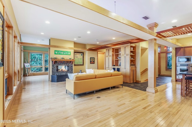 living room with light hardwood / wood-style flooring, ornate columns, and a multi sided fireplace