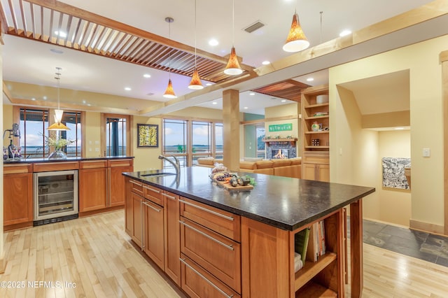 kitchen featuring sink, beverage cooler, a large island with sink, hanging light fixtures, and light hardwood / wood-style floors