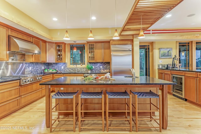 kitchen featuring a center island with sink, a breakfast bar, wall chimney exhaust hood, and appliances with stainless steel finishes