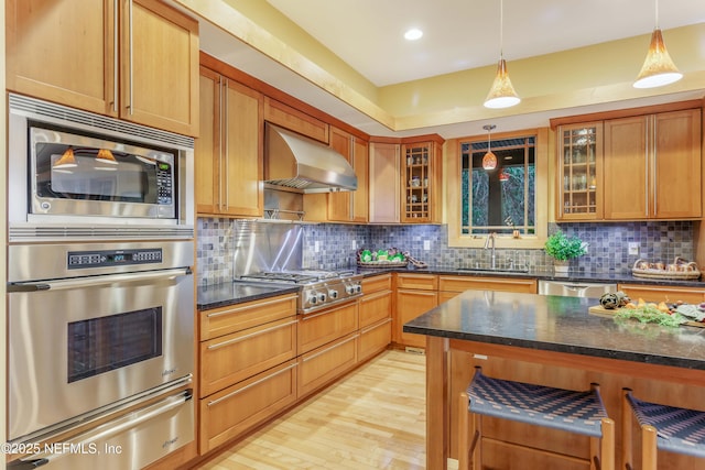 kitchen featuring appliances with stainless steel finishes, sink, dark stone counters, hanging light fixtures, and wall chimney range hood