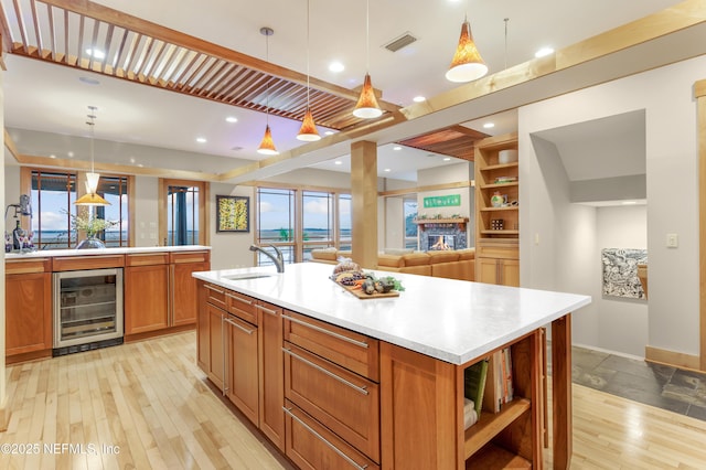 kitchen featuring sink, hanging light fixtures, light hardwood / wood-style flooring, beverage cooler, and a kitchen island with sink