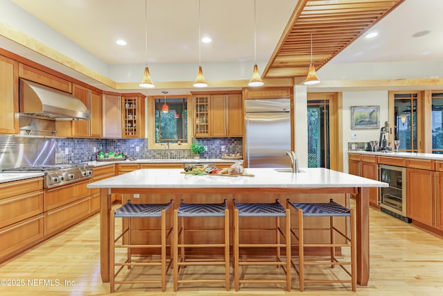 kitchen with an island with sink, stainless steel appliances, a breakfast bar, and wall chimney exhaust hood