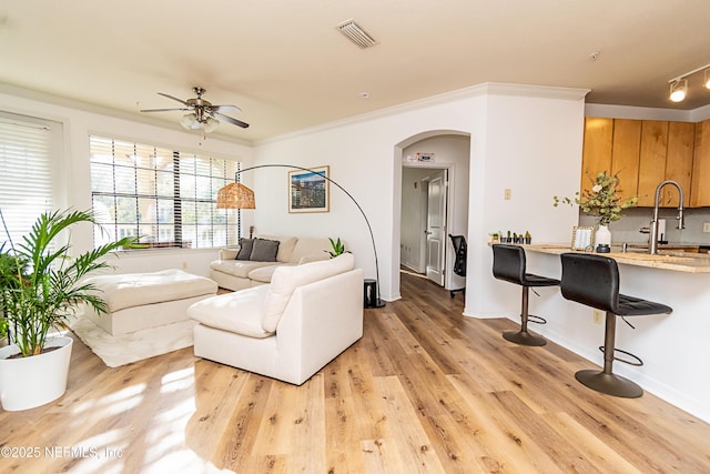 living room with ceiling fan, sink, ornamental molding, and light wood-type flooring