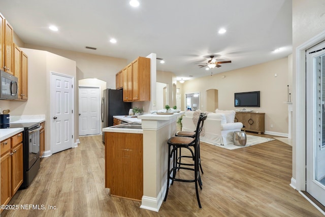 kitchen featuring a kitchen breakfast bar, ceiling fan, light hardwood / wood-style floors, stainless steel refrigerator, and range with electric stovetop