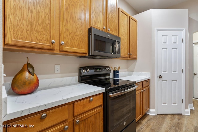 kitchen with black electric range, light hardwood / wood-style flooring, and light stone counters