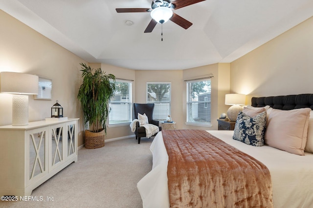 bedroom with ceiling fan, multiple windows, light carpet, and a tray ceiling