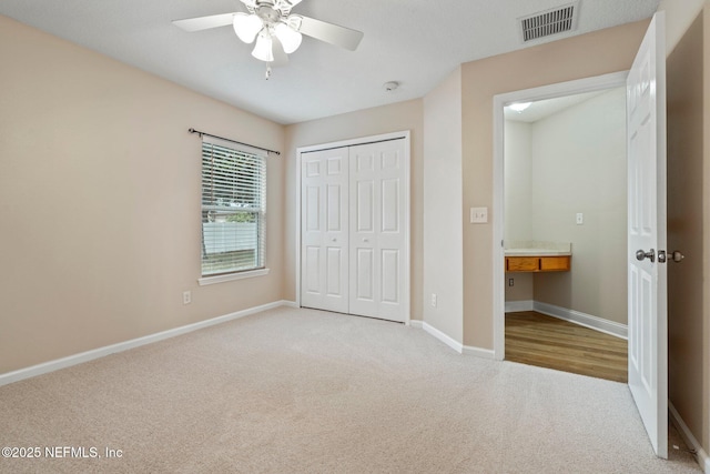 unfurnished bedroom with ceiling fan, built in desk, light carpet, and a closet