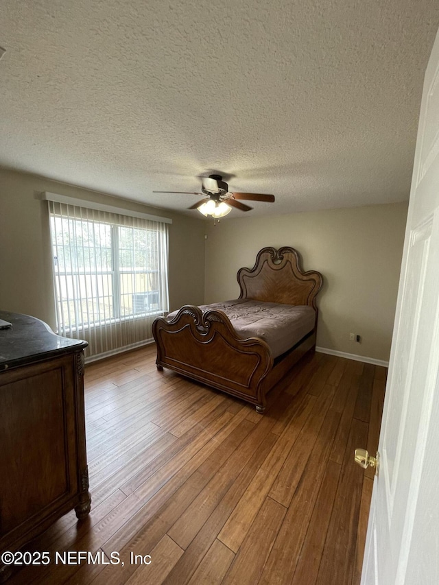 bedroom with ceiling fan, a textured ceiling, wood-type flooring, and baseboards