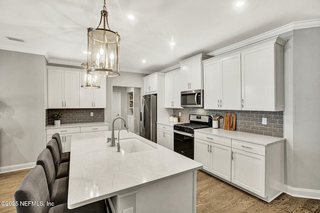 kitchen with stainless steel appliances, sink, white cabinets, hanging light fixtures, and a center island with sink