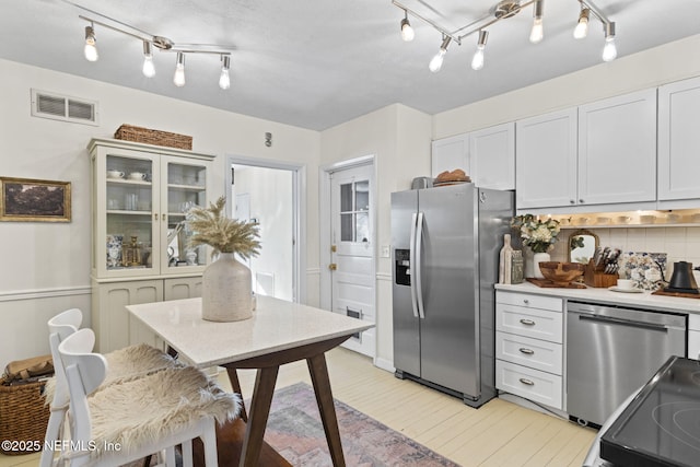 kitchen featuring stainless steel appliances, white cabinets, and backsplash