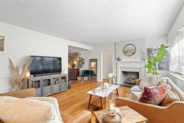 living room featuring wood-type flooring, a large fireplace, and a textured ceiling