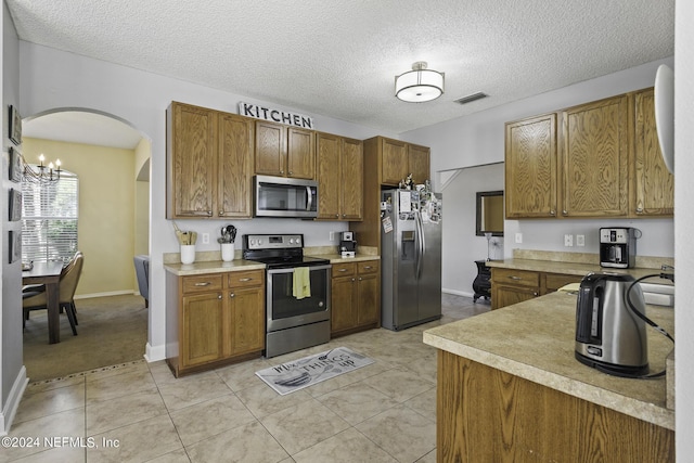 kitchen with stainless steel appliances, light tile patterned floors, a textured ceiling, and an inviting chandelier