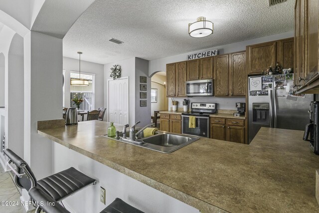 kitchen with pendant lighting, sink, appliances with stainless steel finishes, a kitchen bar, and kitchen peninsula