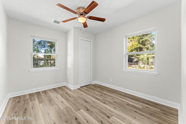 unfurnished bedroom with ceiling fan, light hardwood / wood-style flooring, a closet, and multiple windows