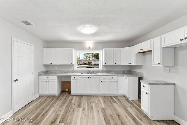 kitchen with sink, white cabinets, a textured ceiling, and light hardwood / wood-style floors