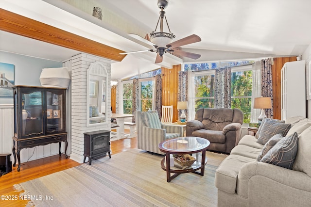 living room featuring ceiling fan, a wood stove, vaulted ceiling with beams, and light hardwood / wood-style floors