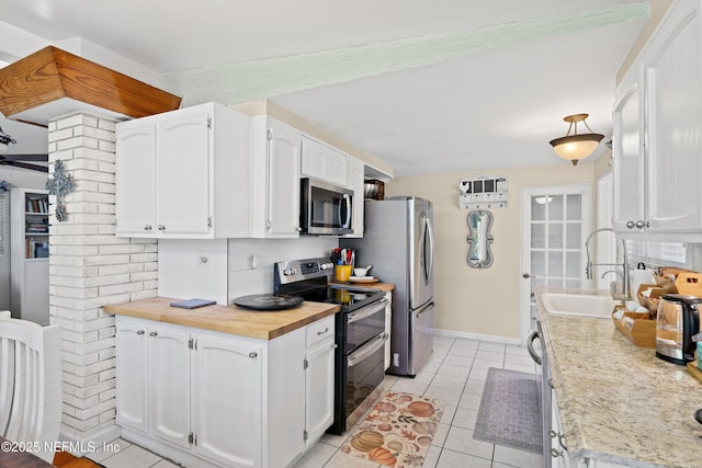 kitchen featuring stainless steel appliances, light tile patterned floors, white cabinets, and wood counters