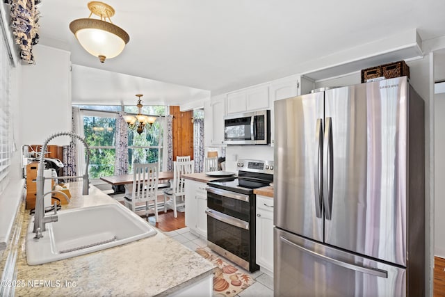 kitchen with sink, appliances with stainless steel finishes, a notable chandelier, white cabinets, and light tile patterned flooring