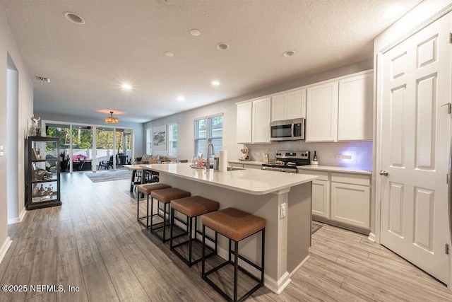 kitchen featuring a kitchen breakfast bar, a center island with sink, appliances with stainless steel finishes, white cabinets, and light hardwood / wood-style flooring