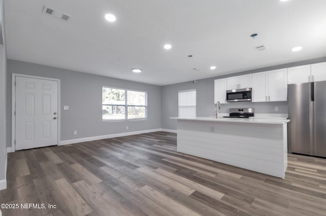 kitchen with a center island with sink, wood-type flooring, stainless steel appliances, sink, and white cabinetry