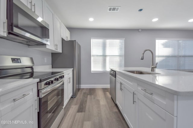 kitchen with sink, white cabinetry, wood-type flooring, light stone countertops, and appliances with stainless steel finishes