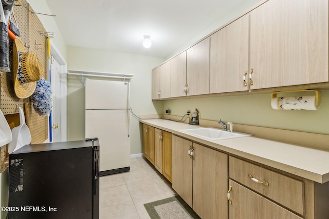 kitchen with light tile patterned floors, white refrigerator, black fridge, light brown cabinets, and sink