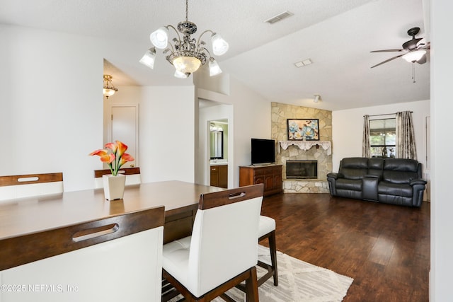 dining area with lofted ceiling, ceiling fan with notable chandelier, dark hardwood / wood-style floors, a textured ceiling, and a stone fireplace