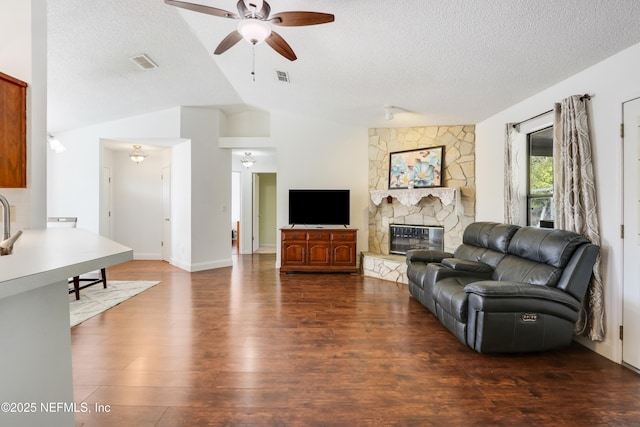 living room featuring dark wood-type flooring, lofted ceiling, a stone fireplace, and a textured ceiling