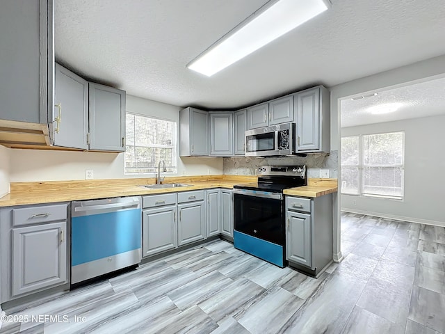 kitchen featuring sink, butcher block countertops, gray cabinetry, a textured ceiling, and appliances with stainless steel finishes