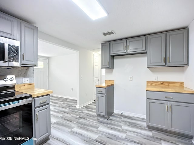 kitchen with appliances with stainless steel finishes, butcher block counters, light wood-type flooring, and gray cabinetry