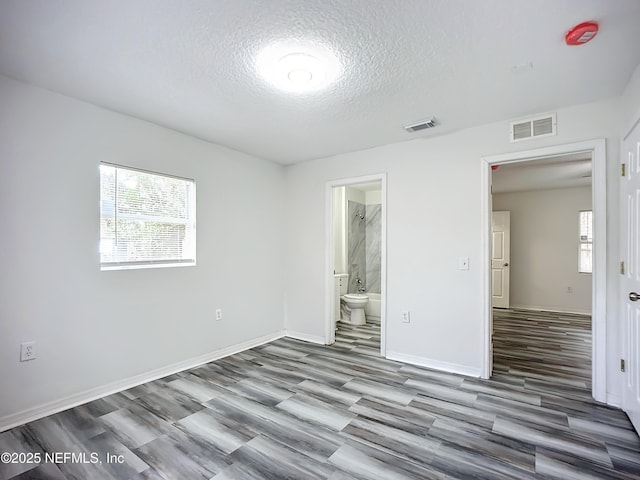 unfurnished bedroom featuring hardwood / wood-style flooring, a textured ceiling, and ensuite bath