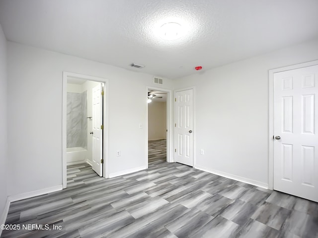 unfurnished bedroom featuring ensuite bath, a textured ceiling, and light hardwood / wood-style floors