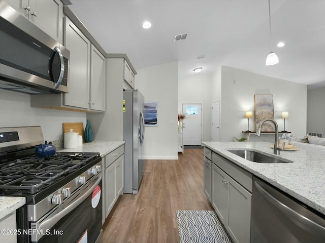 kitchen with pendant lighting, appliances with stainless steel finishes, hardwood / wood-style floors, sink, and gray cabinetry