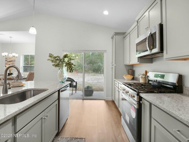 kitchen featuring stainless steel appliances, hanging light fixtures, light stone countertops, vaulted ceiling, and sink